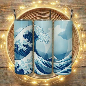 Könnte beinhalten: Drei blaue und weiße isolierte Becher mit einem Wellenmuster, jeweils mit einem silbernen Strohhalm. Die Becher sind mit einem japanisch inspirierten Wellenmuster in Blau- und Weißtönen verziert. Die Becher werden auf einer Holzoberfläche präsentiert.