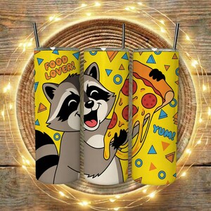 May include: Three yellow insulated tumblers with black straws feature a cartoon raccoon and pizza slice design. The tumblers have the words "FOOD LOVER!" and "YUM!" printed on them. The background is a wooden surface.