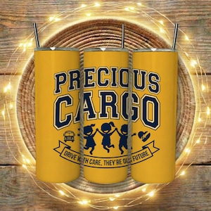 Puede incluir: Tres vasos amarillos con pajitas negras. Los vasos tienen las palabras "PRECIOUS CARGO" en letras de bloque azul marino. Debajo del texto hay siluetas de niños tomados de la mano, un autobús escolar y un corazón. También se incluye el texto "DRIVE WITH CARE, THEY'RE OUR FUTURE".