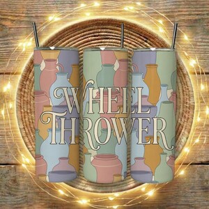 以下が含まれることがあります： パステルカラーの陶器の繰り返し模様が特徴の、蓋とストローが付いたステンレス製のタンブラー3個。「WHEEL THROWER」の文字がタンブラーに縦にプリントされています。タンブラーは、ストリングライトが付いた織りマットの上に置かれています。