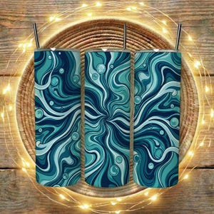 Op de afbeelding: Drie roestvrijstalen bekers met een wervelend abstract ontwerp in blauw en blauwgroen. Elke beker heeft een zilveren rietje. De bekers staan op een gevlochten mand, met lichtslingers en een houten achtergrond.