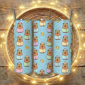 Może przedstawiać: Trzy kubki ze stali nierdzewnej z jasnoniebieskim tłem z powtarzającym się wzorem kreskówkowych kapibar noszących opaski na głowę w spa i owiniętych ręcznikami. Żółte gumowe kaczki i bąbelki również znajdują się we wzorze.