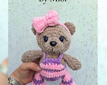 Op de afbeelding: Een handgemaakte bruine teddybeer met roze en paarse gestreepte overalls en een bijpassende strik. De beer heeft zwarte ogen en een zwarte neus. De tekst "Bear in Overalls" en "by Mi6i" is zichtbaar.