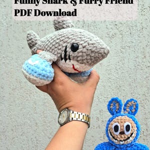 May include: A gray and white crocheted shark with black accents and blue flippers is held in a hand. A blue crocheted bunny with a smiling face is held in another hand. The text "2 Crochet Patterns Funny Shark & Furry Friend PDF Download" is at the top.