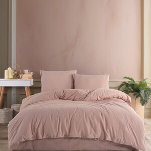 Può includere: Un copripiumino rosa cipria con chiusura a bottoni e due federe abbinate. La biancheria da letto è su un letto con pavimento in legno.
