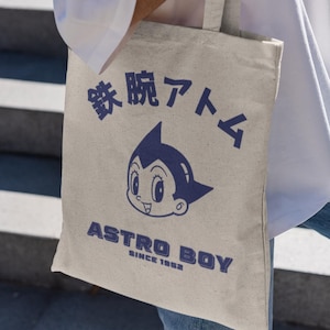 May include: A beige tote bag with a blue Astro Boy graphic and the text "鉄腕アトム" and "ASTRO BOY SINCE 1963".