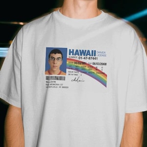 May include: A white short-sleeve t-shirt featuring a graphic print of a Hawaii driver licence for McLovin. The licence includes a portrait, the text HAWAII DRIVER LICENCE, number 01-47-87441, a rainbow stripe, and address details for 892 Momona St, Honolulu, HI.