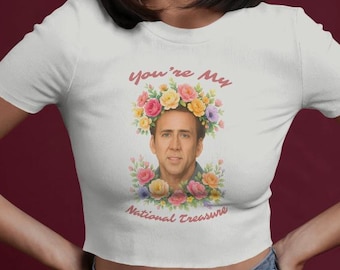 May include: White crop top featuring a watercolor image of Nicolas Cage with a floral crown. The text "You're My National Treasure" is printed above and below the image in a cursive font. The model is wearing black sunglasses.