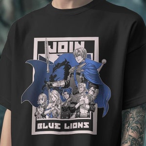 Puede incluir: Camiseta negra con un gráfico blanco de personajes del videojuego Fire Emblem: Three Houses. El gráfico presenta el texto "JOIN BLUE LIONS".