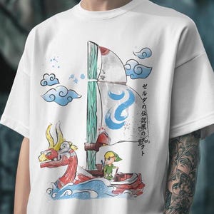 Puede incluir: Camiseta blanca con un gráfico de Link de The Legend of Zelda: The Wind Waker navegando en un barco con una cabeza de dragón roja. El texto "ゼルダの伝説 風のタクト" está escrito en japonés en el lado derecho de la camiseta.