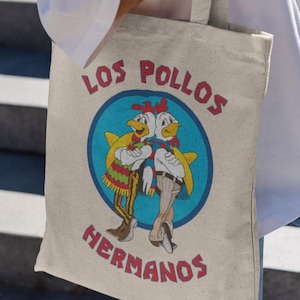 May include: A white canvas tote bag featuring a blue circle with two cartoon chickens. The text "Los Pollos Hermanos" is printed in red and yellow.
