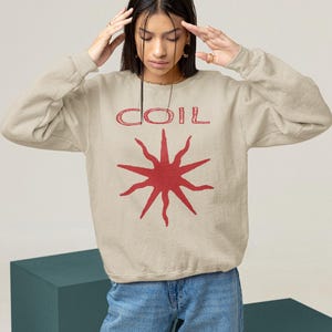 May include: A beige sweatshirt with a red graphic of a sun with the word "COIL" above it.