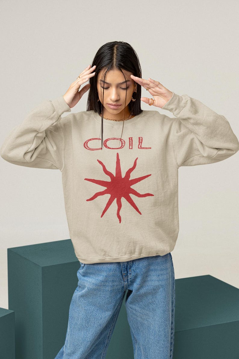 May include: A beige sweatshirt with a red graphic of a sun with the word "COIL" above it.