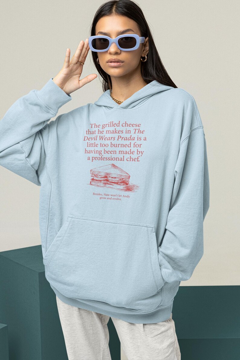 May include: Light blue hooded sweatshirt with a graphic print of a grilled cheese sandwich and the text "The grilled cheese that he makes in The Devil Wears Prada is a little too burned for having been made by a professional chef. Besides, Nate won't let Andy grow and evolve."