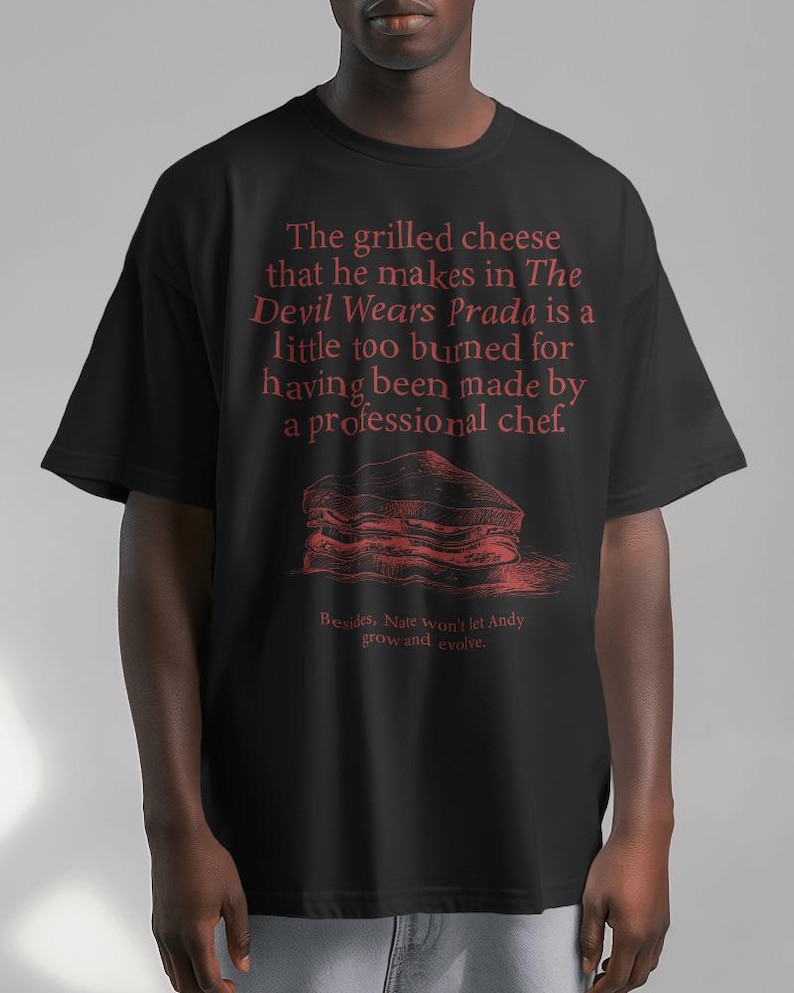 May include: Black t-shirt with a red graphic print of a grilled cheese sandwich and text that reads "The grilled cheese that he makes in The Devil Wears Prada is a little too burned for having been made by a professional chef. Besides, Nate won't let Andy grow and evolve."