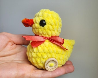 May include: A handmade yellow plush duck with an orange beak and a red ribbon tied around its neck. The duck has a small wooden button on its base that says "Handmade with love".