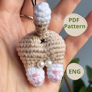 Può includere: Schema di amigurumi all'uncinetto per il sedere di un gatto con coda bianca, corpo beige e zampe rosa. Lo schema è disponibile in inglese e include un download PDF.