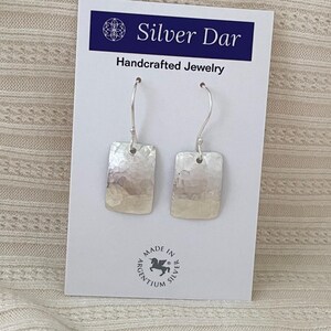 May include: A pair of silver rectangular drop earrings with a hammered texture on a white display card labeled Silver Dar Handcrafted Jewelry with a Made in Argentium Silver logo at the bottom center of the card.