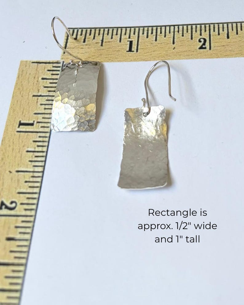 May include: Two silver-toned earrings with hammered rectangular drops and curved ear wires. A wooden ruler shows the earrings are approximately 0.5 inches wide and 1 inch tall, as noted by the text: Rectangle is approx. 1/2" wide and 1" tall.