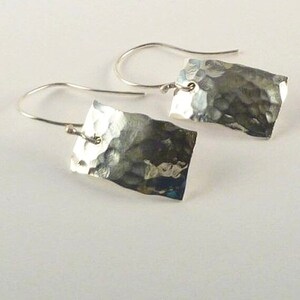 May include: A pair of silver-toned drop earrings featuring rectangular metal pendants with a hammered, textured surface. Each pendant is suspended from a curved silver-toned ear wire, creating a simple and reflective metallic design.