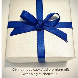 May include: A square gift box wrapped in smooth white paper, tied with a vibrant royal blue satin ribbon formed into a centered bow. Below the box, the text reads: Gifting made easy. Add premium gift wrapping at checkout.