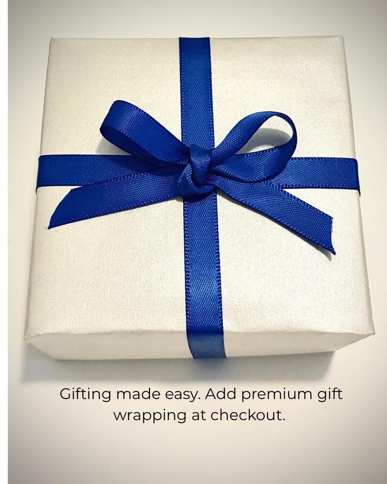 May include: A square gift box wrapped in smooth white paper, tied with a vibrant royal blue satin ribbon formed into a centered bow. Below the box, the text reads: Gifting made easy. Add premium gift wrapping at checkout.