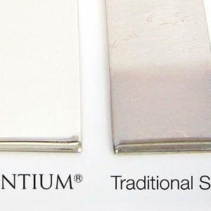 May include: Two rectangular metal strips placed side by side. The left strip is labeled ARGENTIUM and appears bright and reflective. The right strip is labeled Traditional Sterling and has a slightly darker, muted metallic finish.
