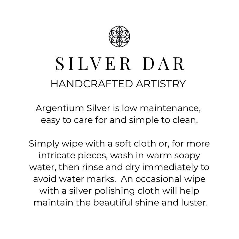 May include: A white informational card featuring a black circular logo with a floral design at the top. The text reads: SILVER DAR HANDCRAFTED ARTISTRY. Below, instructions explain that Argentium Silver is low maintenance and easy to clean by wiping with a soft cloth or washing in warm soapy water, rinsing, and drying immediately to avoid water marks.