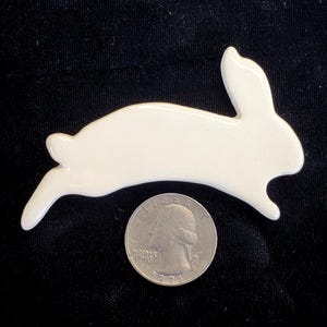May include: White ceramic rabbit figurine in a leaping pose. The figurine is about the size of a quarter.