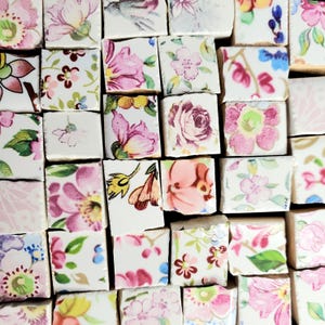 May include: A collection of small, square ceramic tiles with a white background and floral patterns in shades of pink, green, and yellow.