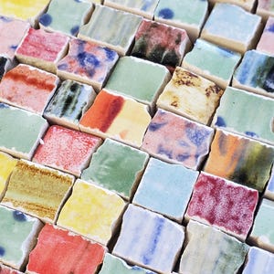 May include: A close-up of a mosaic tile sheet made of small, square tiles in various colors, including red, green, blue, yellow, and white. The tiles are arranged in a staggered pattern, creating a visually interesting texture.