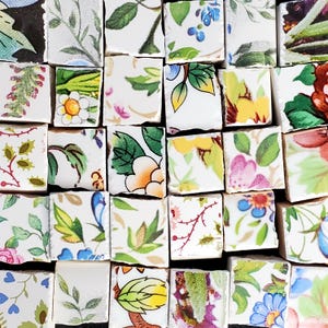 May include: A collection of small, square ceramic tiles with a white background and floral patterns in shades of green, pink, yellow, and blue.