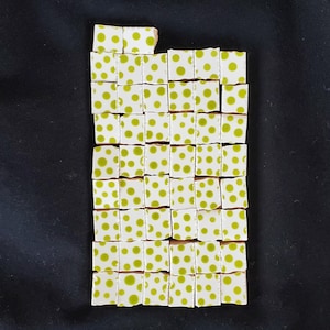 May include: A collection of forty-seven small, square ceramic tiles arranged in a rectangular grid. Each tile features a white background with a single, centered lime green polka dot. The tiles are uniform in size and shape, displaying a consistent pattern.
