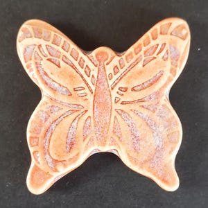 May include: A ceramic butterfly figurine in shades of peach and cream. The butterfly has detailed wing patterns and a textured surface. The figurine is a decorative item.