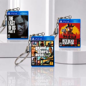 Può includere: Tre portachiavi rettangolari in miniatura con le copertine dei giochi PlayStation 4 The Last of Us Part II, Grand Theft Auto V e Red Dead Redemption II. Ogni portachiavi ha un bordo in plastica blu, una catenella e un anello.