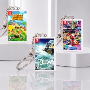 Puede incluir: Tres llaveros rectangulares con portadas de juegos de Nintendo Switch en miniatura para Animal Crossing New Horizons, The Legend of Zelda Tears of the Kingdom y Mario Kart 8 Deluxe. Cada llavero tiene una anilla y cadena de metal plateado.