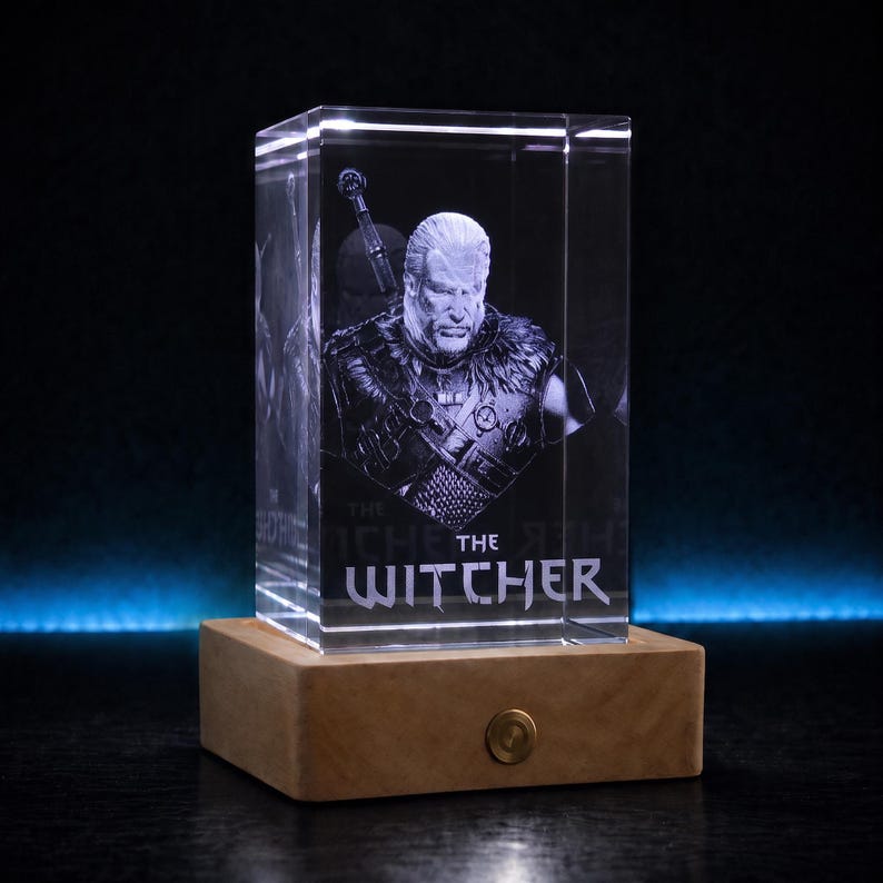 Pu&ograve; includere: Un blocco di vetro trasparente rettangolare con un ritratto 3D inciso al laser di un uomo con capelli lunghi e una spada sulla schiena. Il testo THE WITCHER &egrave; inciso in basso. Il blocco di vetro poggia su una base in legno chiaro con un pulsante.