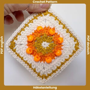 Puede incluir: Un patrón de ganchillo cuadrado en blanco, amarillo mostaza y naranja. El centro presenta un diseño floral con cuentas naranjas. El borde es amarillo mostaza. El texto "Crochet Pattern" y "PDF english" son visibles.