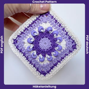 Peut inclure: Un motif de crochet carré aux tons de violet, lavande et blanc, orné de perles lavande. Le motif présente un motif floral central et une bordure blanche texturée. Le texte en haut indique "Crochet Pattern".