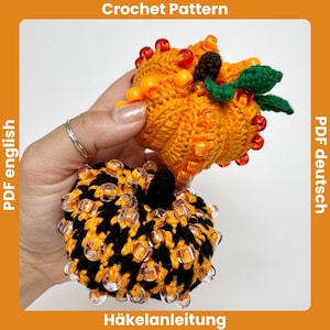 May include: Two crocheted pumpkins, one orange and one black and orange, are shown. The orange pumpkin is topped with green leaves and orange beads. The black and orange pumpkin is covered in clear beads. The words "Crochet Pattern" and "Häkelanleitung" are at the top and bottom.
