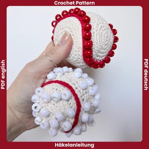 Könnte beinhalten: Zwei gehäkelte Bälle mit roten und weißen Akzenten. Ein Ball hat rote Perlen am Rand, der andere weiße Perlen. Der Text "Crochet Pattern" steht oben, und "PDF english" steht links. Der Text "Häkelanleitung" steht unten.