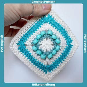 Peut inclure: Un carré crocheté blanc et turquoise, orné de perles turquoise. La pièce présente un motif géométrique et est tenue par une main. Le texte en haut indique "Crochet Pattern".