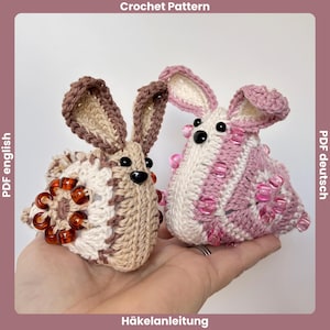 Könnte beinhalten: Zwei gehäkelte Hasenfiguren. Einer ist beige und weiß mit braunen Akzenten und bernsteinfarbenen Perlen. Der andere ist rosa und weiß mit rosa Perlen. Die Hasen haben schwarze Augen und große Ohren. Der Text "Crochet Pattern" und "Häkelanleitung" sind sichtbar.