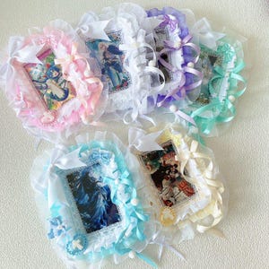 May include: A selection of framed art pieces with decorative lace and ribbon. Each frame features a different image and is adorned with bows, pearls, and crosses. The colour palette includes pink, blue, purple, green, and yellow. The frames are trimmed with frills.