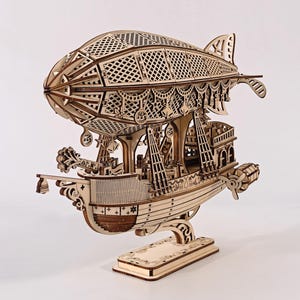 Può includere: Un modello in legno tagliato al laser di un dirigibile in stile steampunk, caratterizzato da un grande pallone con motivo a reticolo fissato a un ponte inferiore dettagliato con ringhiere complesse, piccole eliche e un supporto decorativo.