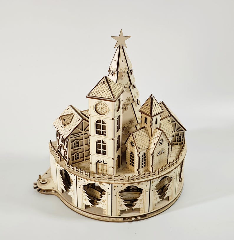 May include: A wooden Christmas village model with a clock tower, houses, and a Christmas tree topped with a star. The model is made of light-colored wood and features intricate cut-out details, creating a festive and decorative item.