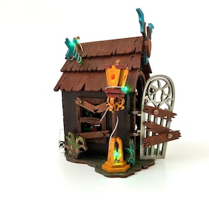 May include: A miniature haunted house with a brown shingled roof, a broken window, and a decorative gate. The house has a lamppost with a glowing green light and is decorated with green and orange lights.