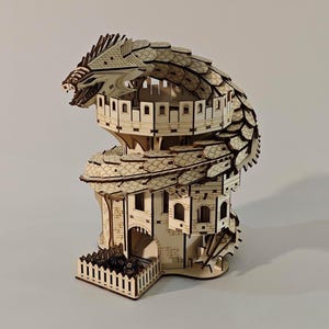 May include: A wooden dragon-themed dice tower. The tower is constructed from light-colored wood and features a dragon's head at the top, with the body wrapping around the tower. The tower has multiple levels with small windows and a dice tray.