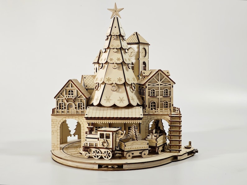 May include: A wooden Christmas village scene with a train, buildings, and a large Christmas tree. The tree is topped with a star. The train has a locomotive and two cars. The buildings include a clock tower and houses.