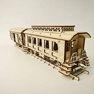 Könnte beinhalten: Detailliertes Holzmodell eines Personenwaggons. Das Modell verfügt über aufwendige Ausschnitte für Fenster und Türen mit sichtbaren Innendetails. Der Waggon steht auf einem Holzgleis und zeigt die Handwerkskunst der Miniaturreplik.